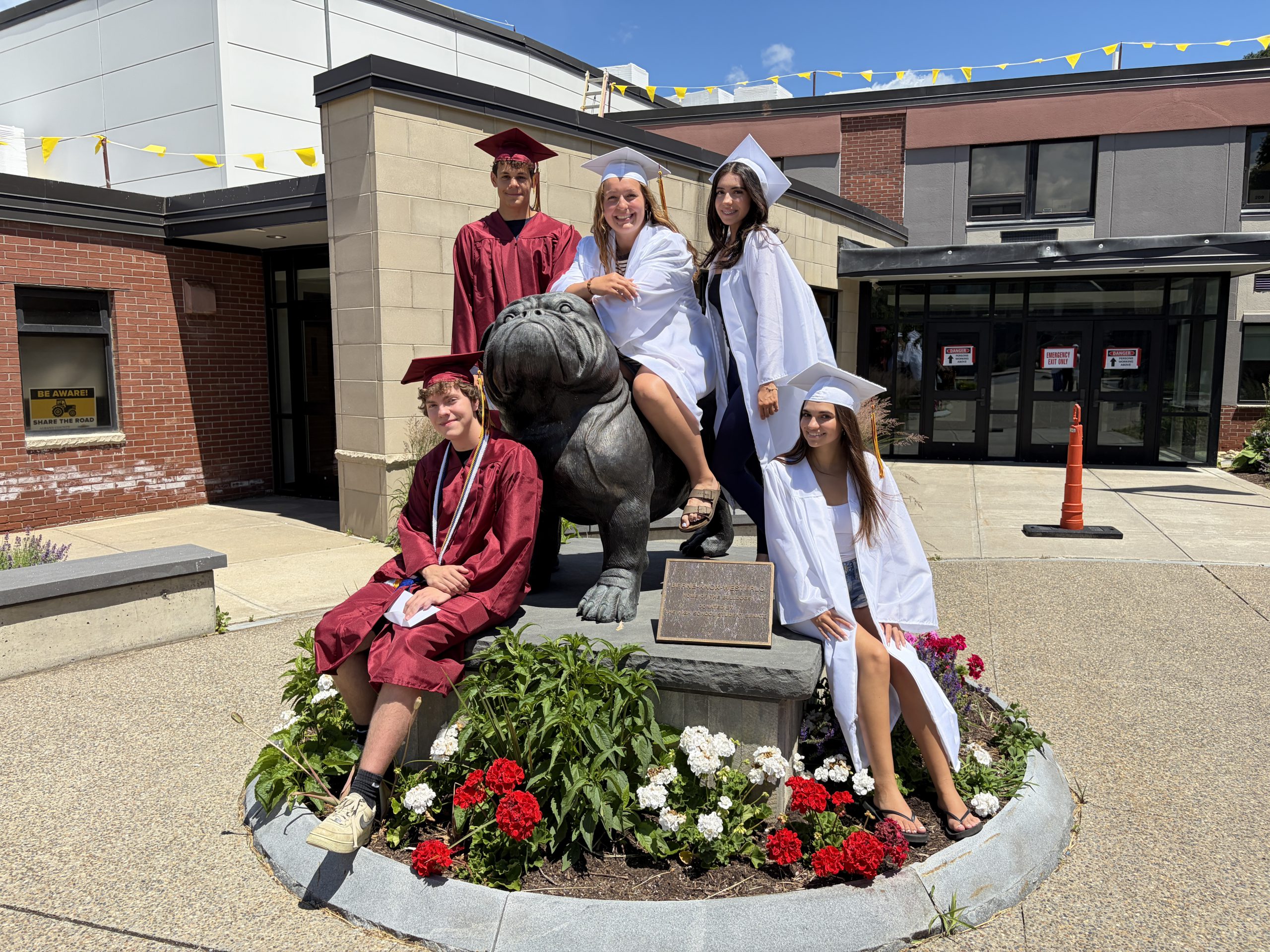 Students in graduation caps and gowns surround a bulldog statue outside the high school