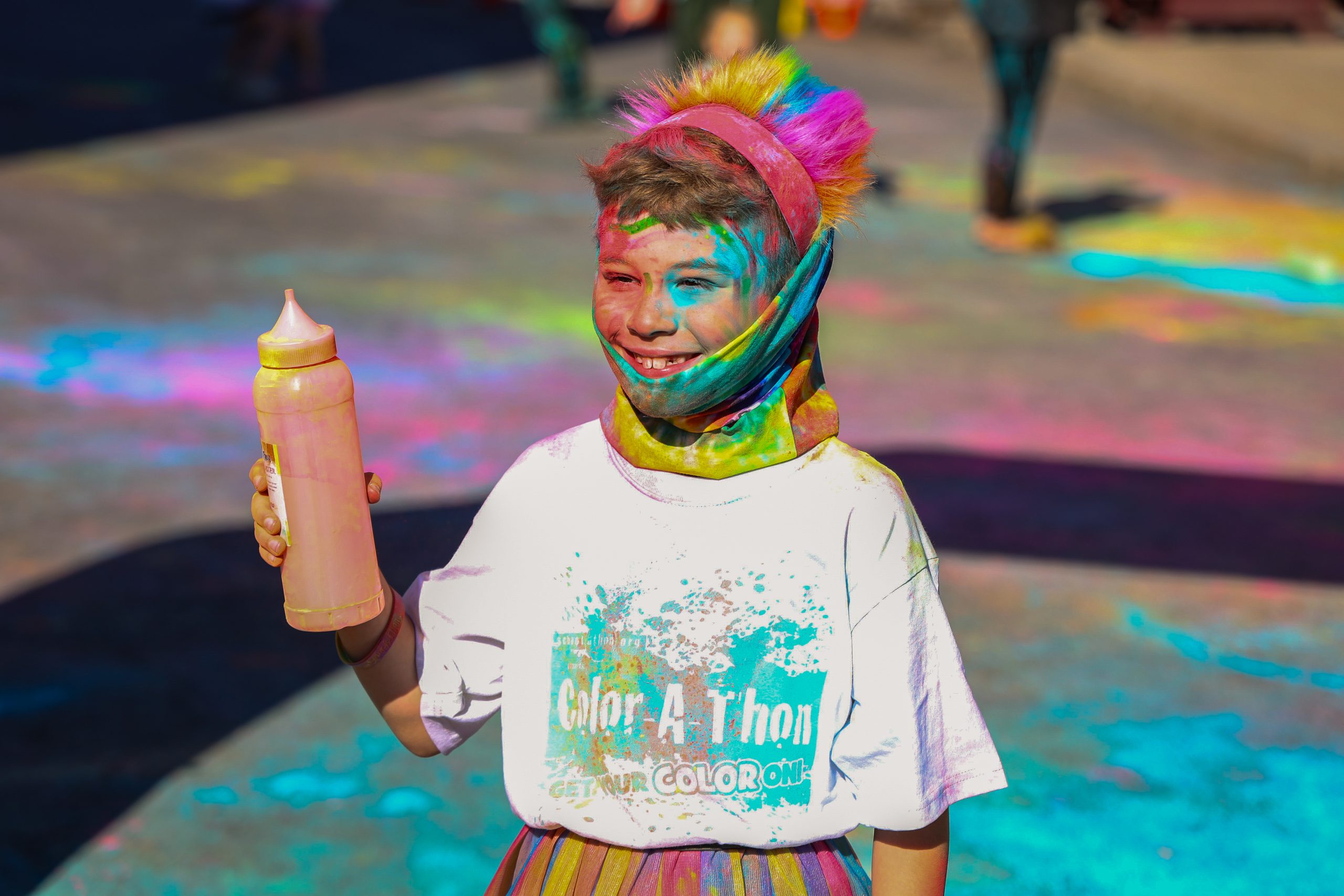 Elementary student in rainbow colors holding a bottle of color run color