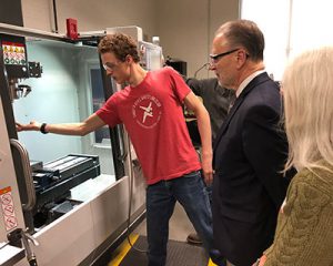 student in t-shirt and safety glasses shows a machine to man in suit