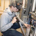 boy in cap works on a air conditioning unit