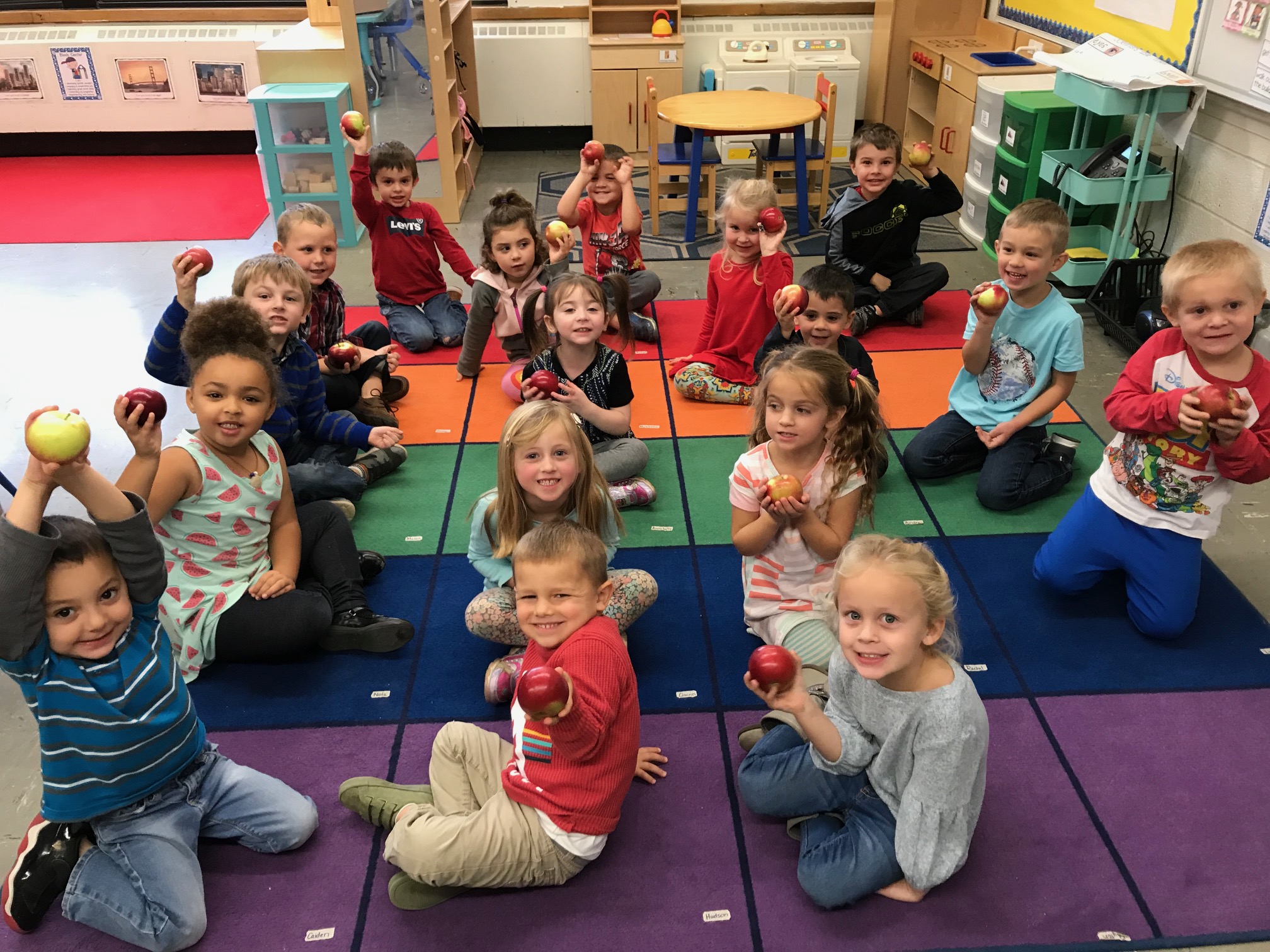 pre K class sits on floor showing off their shiny apples