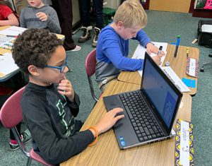 student works on computer while student next to him draws a race bot racetrack