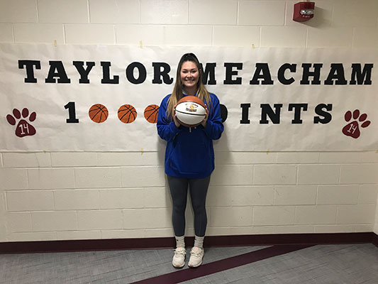 Taylor Meacham holding basketball in front of banner