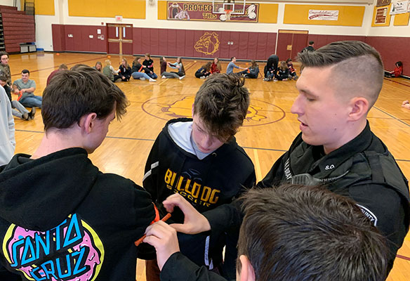 Officer Bray instructs two students on how to apply a tourniquet