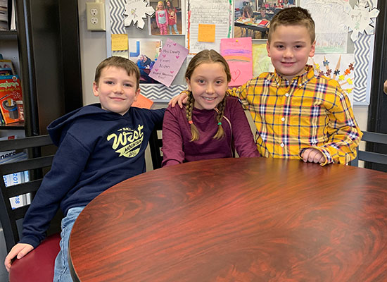 3 second graders, two boys and one girl, sit together at table