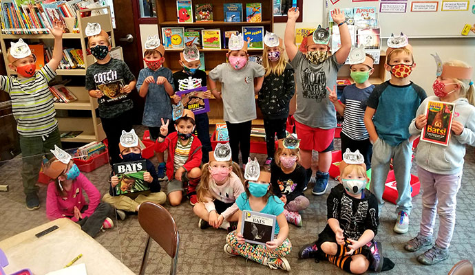 students holding books and wearing paper bat hats