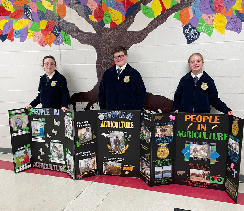 3 students wearing FFA jackets stand with display boards