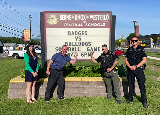 4 people standing in front of BKW school sign showing Badges vs Bulldogs