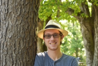 boy with hat standing next to a tree