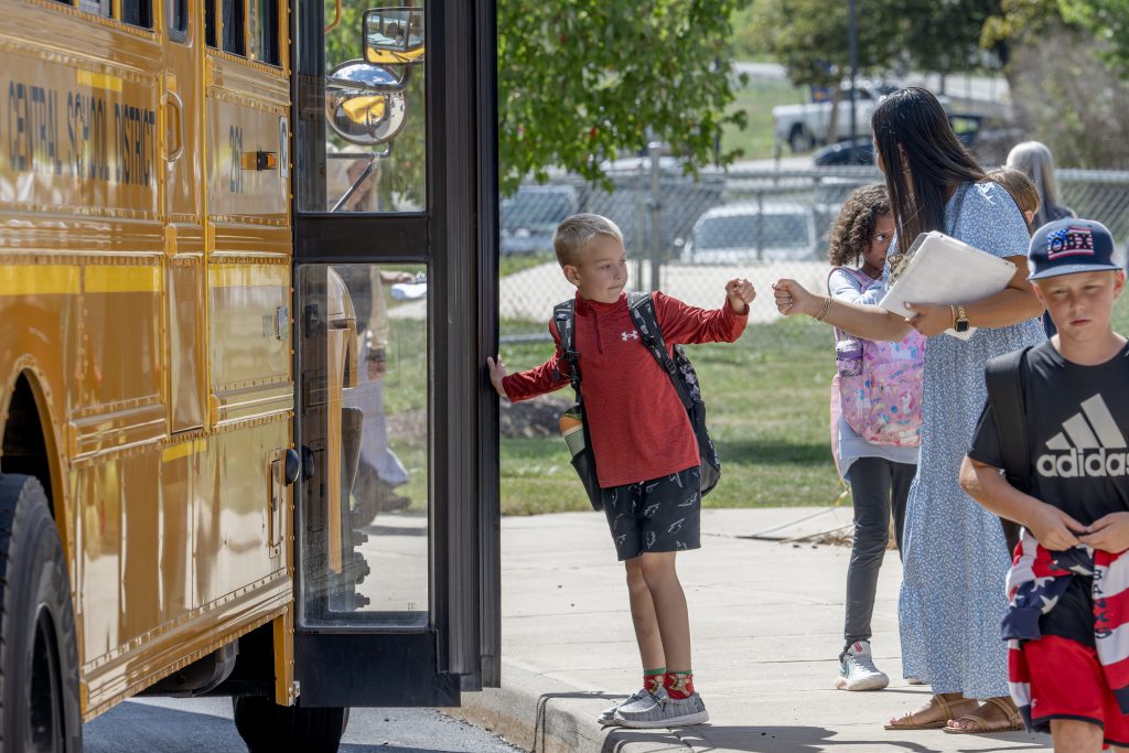 young student fist bumping teacher before getting onto bus