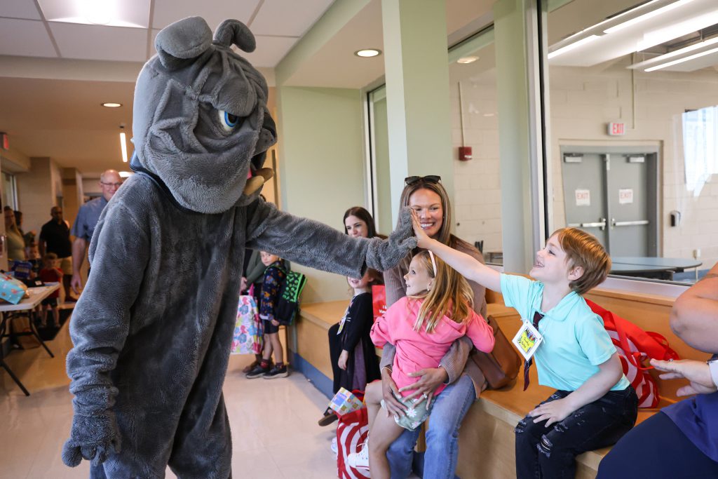 bernie bulldog mascot high-fiving young student in hallway with other students around, all smiling