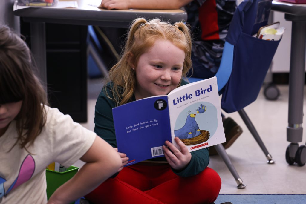 young student holding and reading a book called little bird