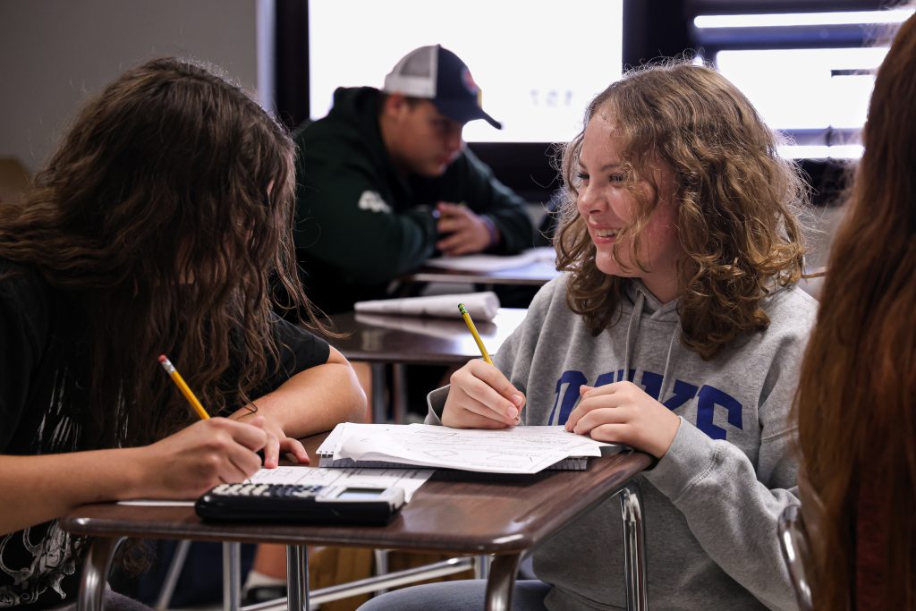 students laughing and smiling, working on homework in class