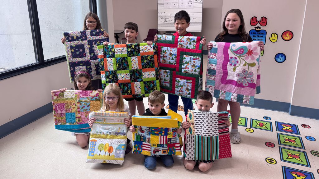 Seven students smiling holding quilts