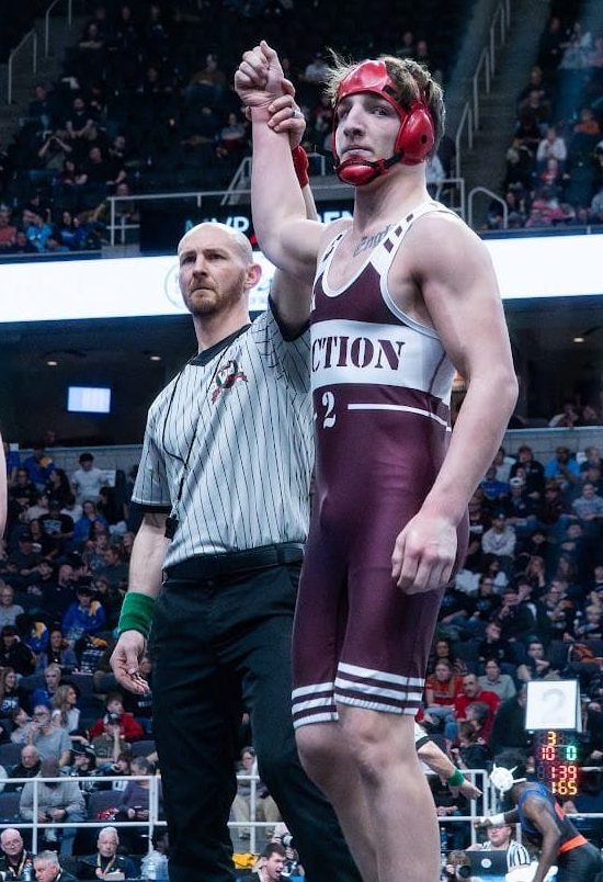 A referee holds a teen wrestlers arm up overhead to announce his victory on the mat