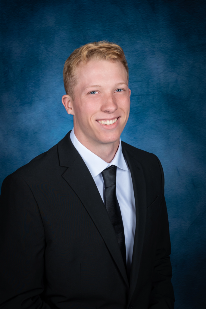 Smiling teen wearing a black suit, white collared shirt, and black neck tie.