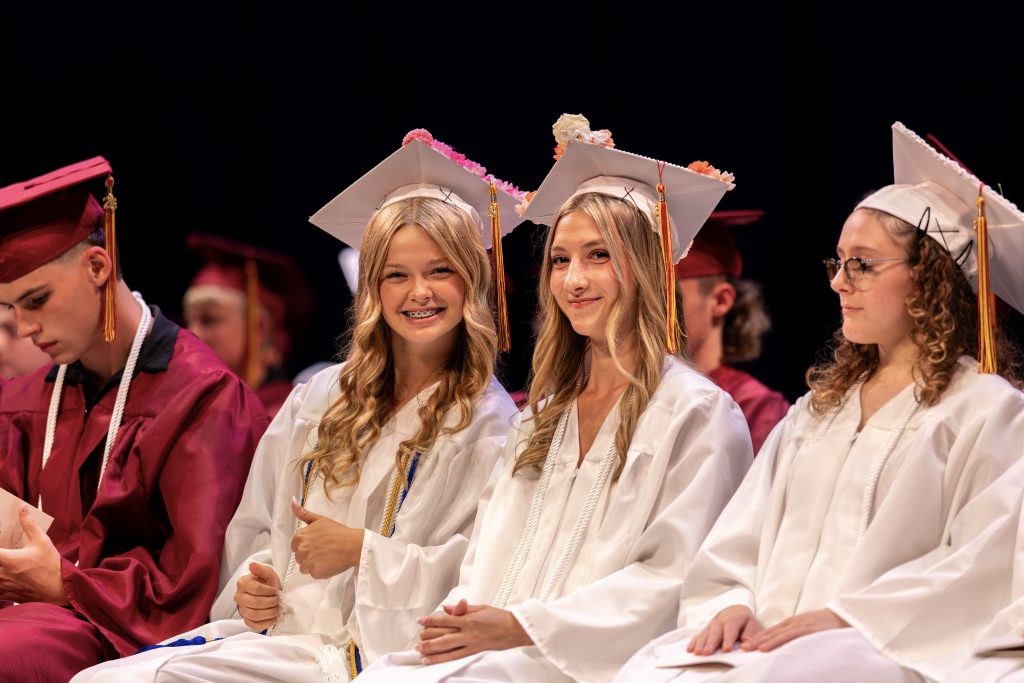 Three students sitting on stage at graduation smiling on stage