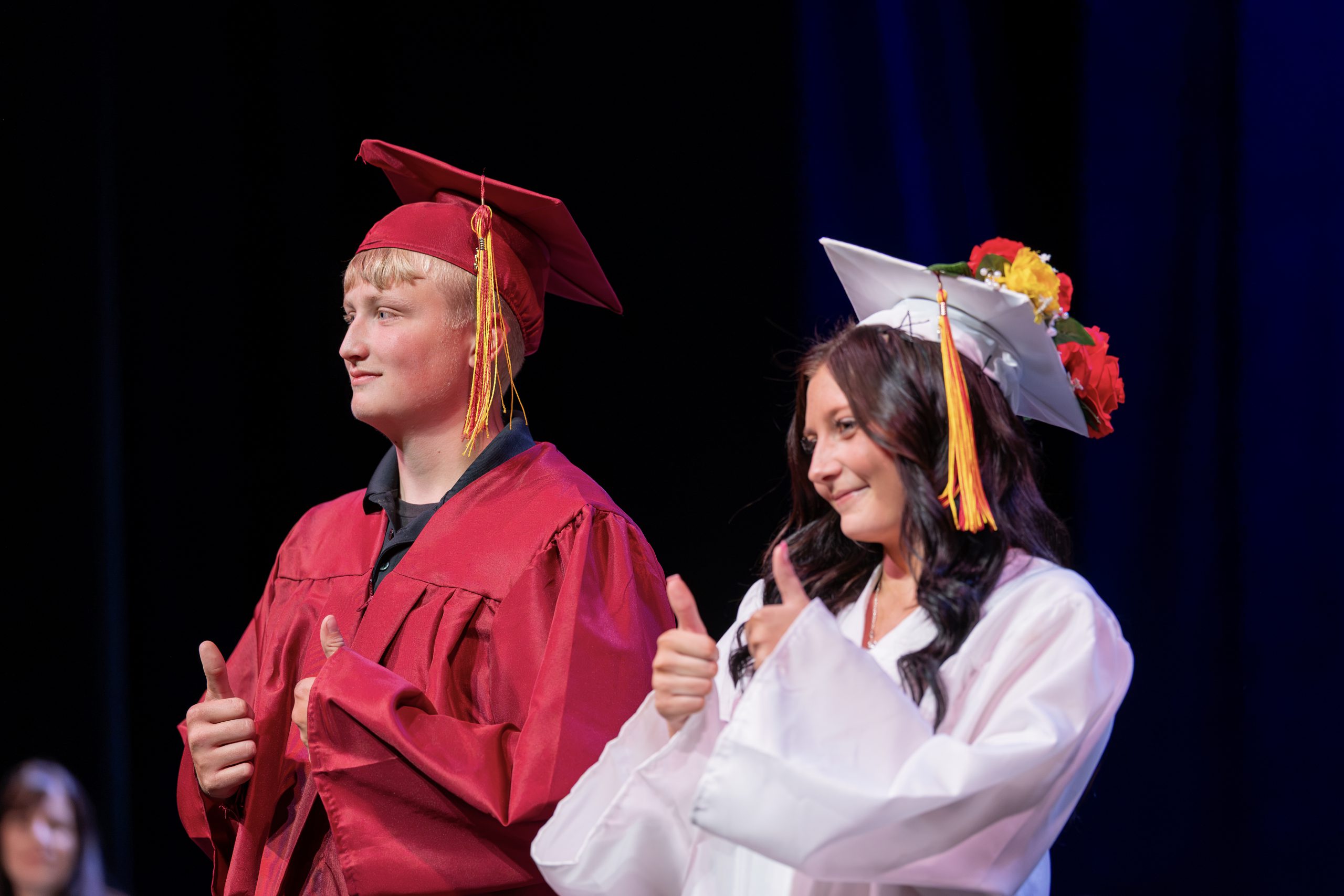 Two students in traditional graduation caps and robes give a thumbs up.