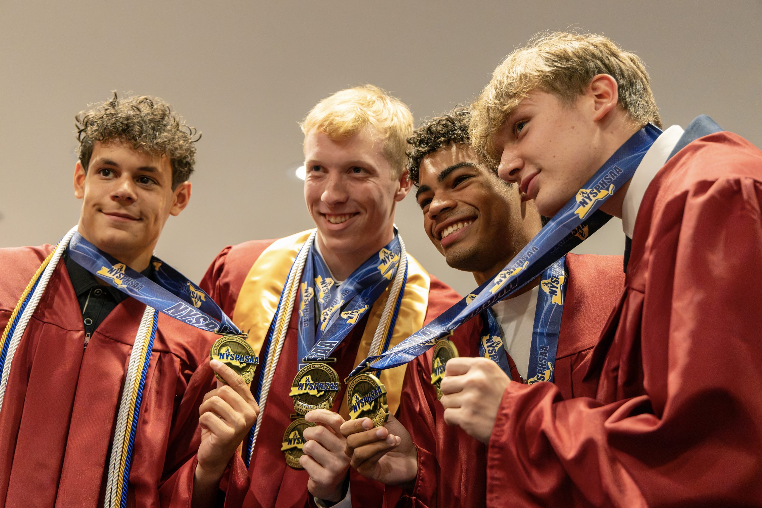 Four students in red graduation robes holding their medals and smiling