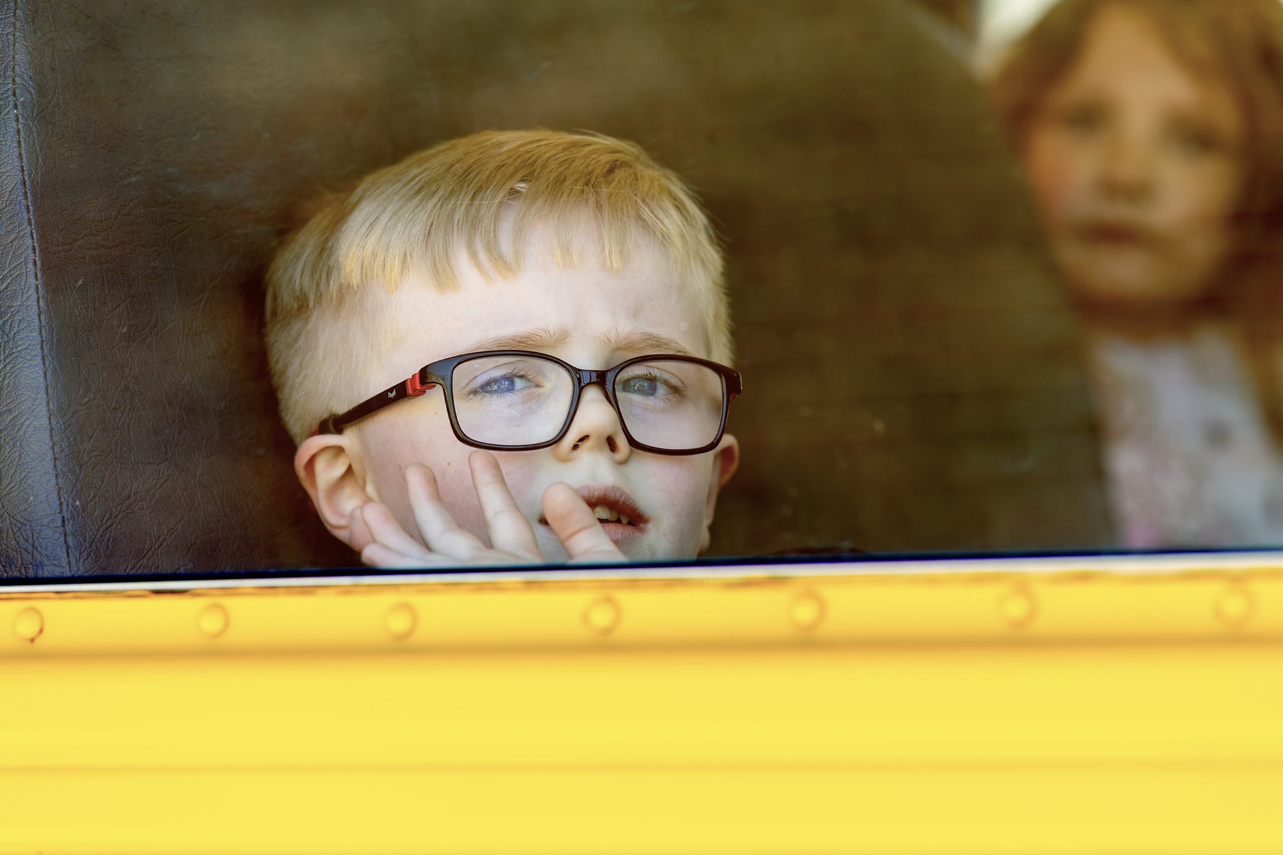 A young student wearing glasses looks out the bus window