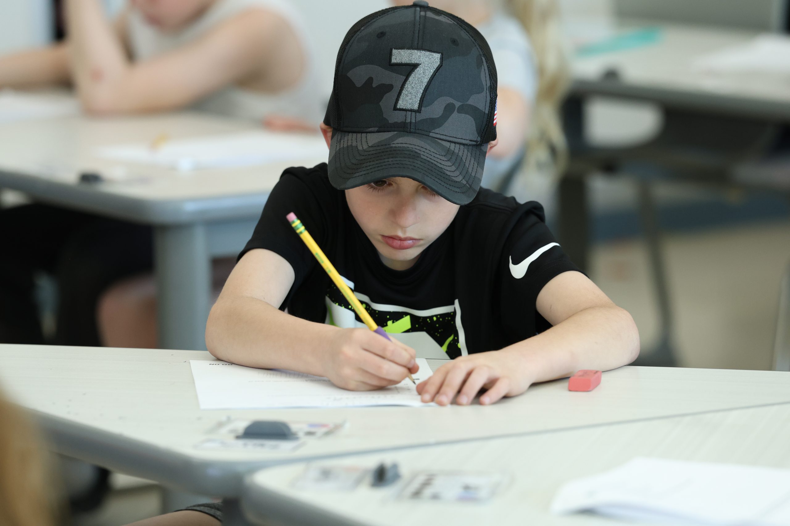 A student sits at a desk and writes with a pencil