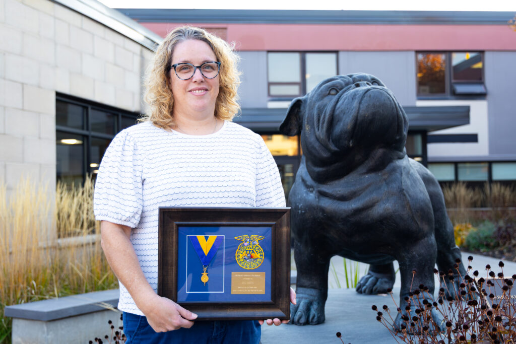 Erin Smith smiling by the bulldog statue holding her FFA Honorary American Degree award